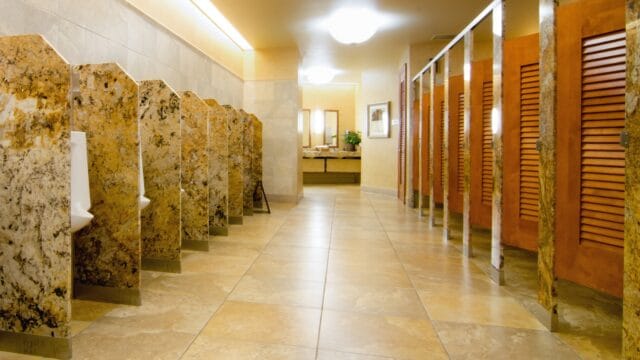 Custom shape stone urinal screens and louvered partition doors in a commercial restroom.