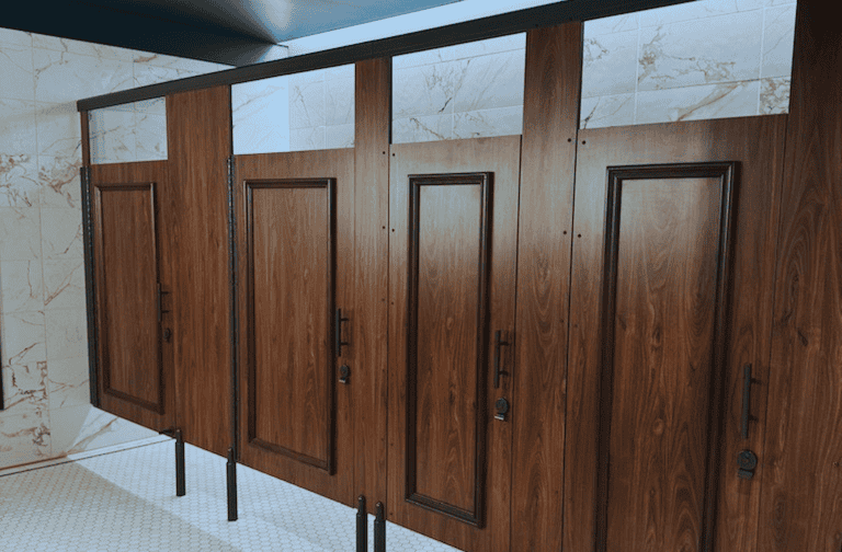 Row of closed wooden bathroom stalls with marble tile walls and a tiled floor.
