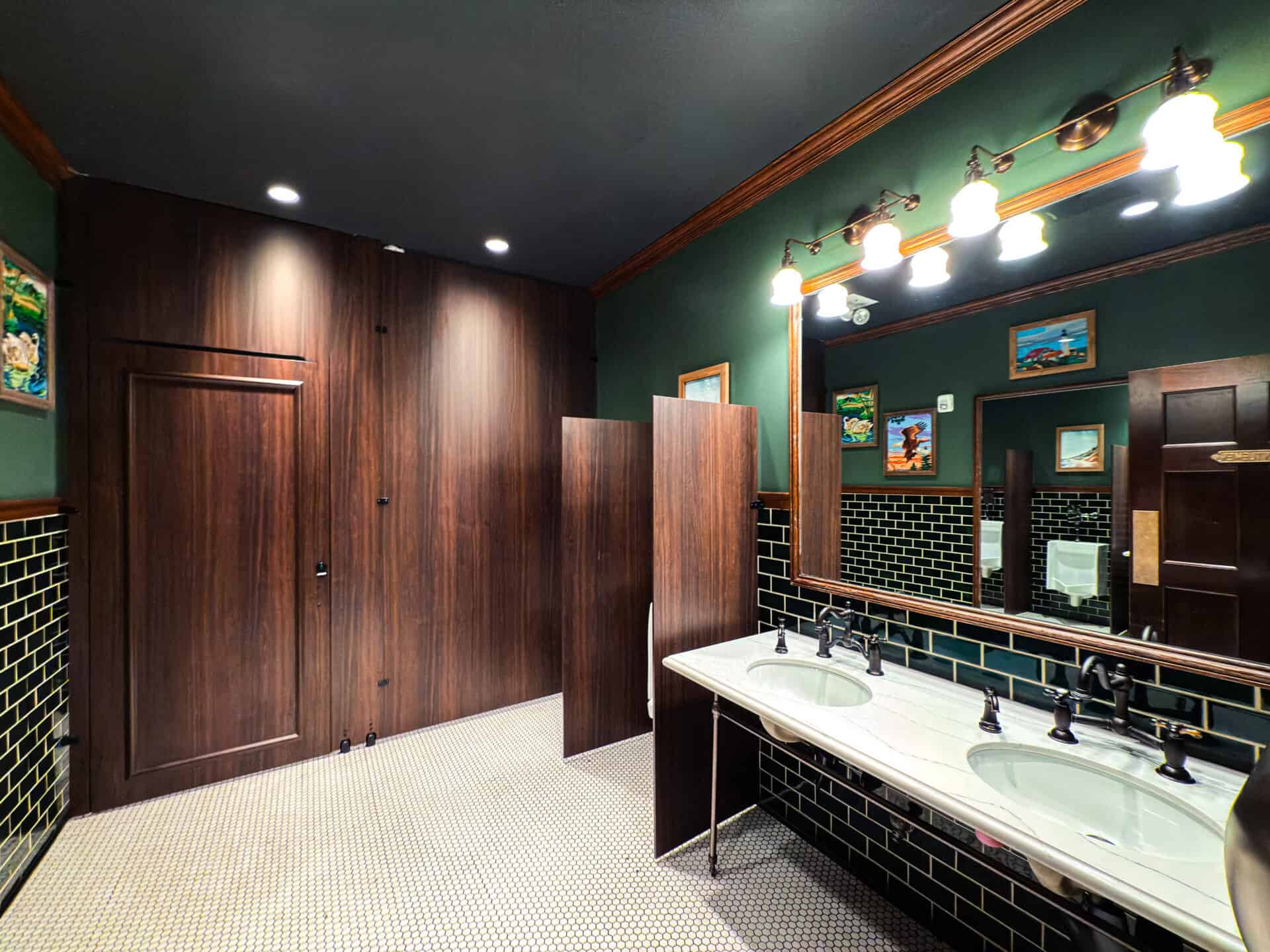 Floor To Ceiling toilet partitions in Wilsonart Colombia Walnut compact laminate with zero sightline and black powder-coated hardware for an entertainment venue application. Image by Ironwood Manufacturing.