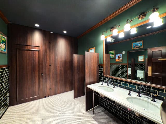 Floor To Ceiling toilet partitions in Wilsonart Colombia Walnut compact laminate with zero sightline and black powder-coated hardware for an entertainment venue application. Image by Ironwood Manufacturing.