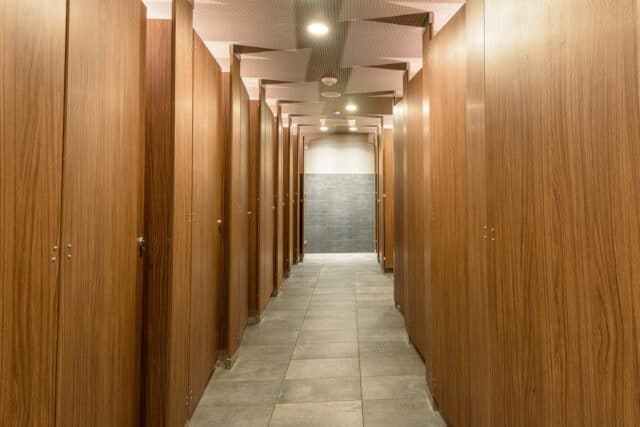 Commercial restroom with full-height restroom partitions made from laminate material, mounted from floor to ceiling for maximum privacy.