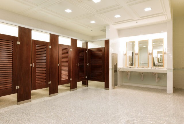 Spacious public restroom with wooden stall doors, mirrors, sinks, and tiled floor under bright ceiling lights.