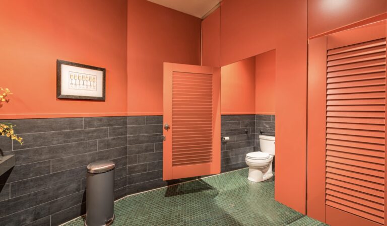 Picture of a bright orange public restroom partition with a louvered door, mounted ceiling hung.