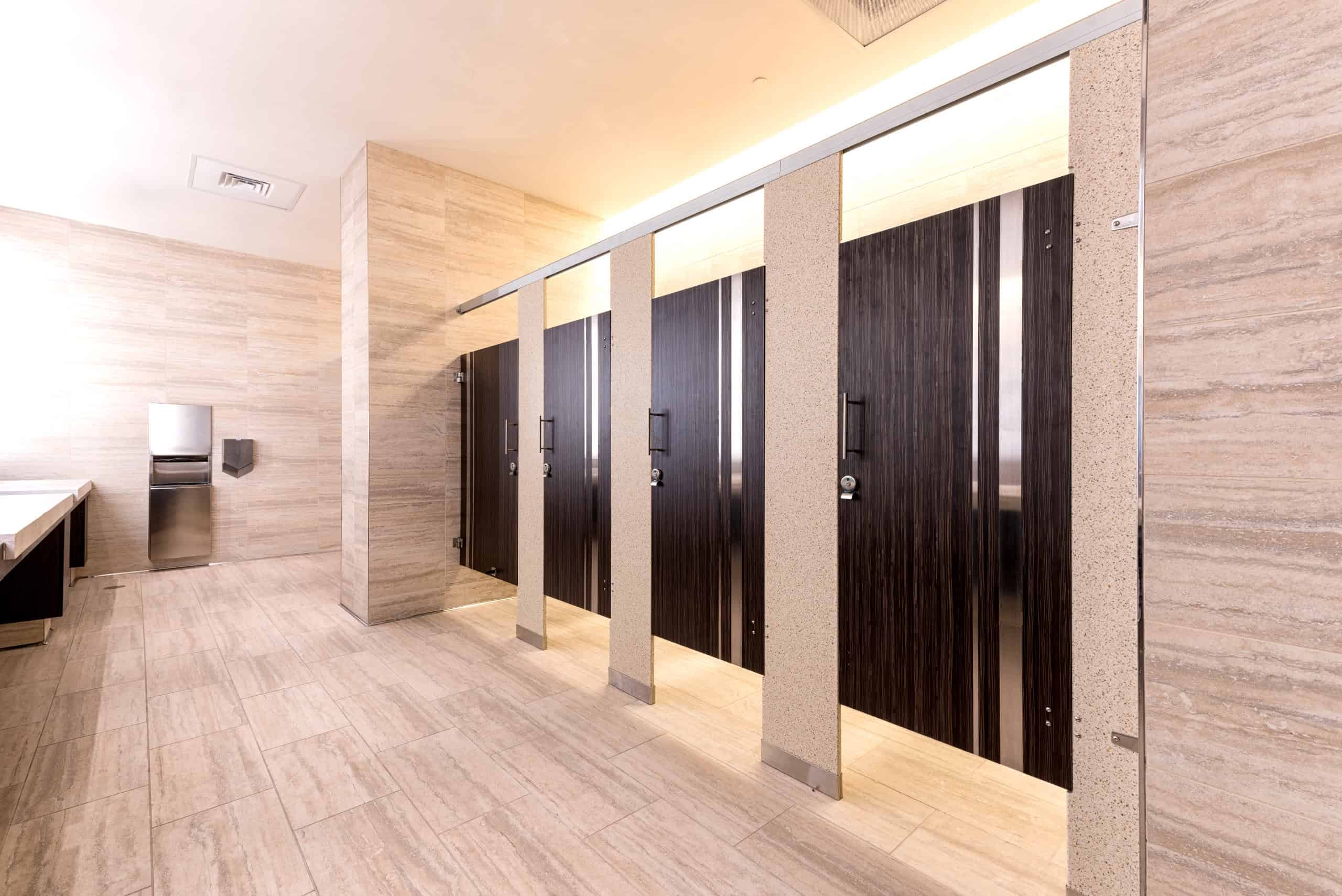 A modern restroom with wooden stall doors, beige tiled walls and floors, and a countertop on the left.