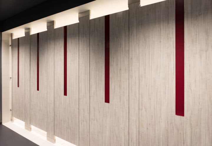 A commercial upscale restroom featuring partitions with high pressure laminate woodgrain doors and pilasters. Floor to ceiling mounted with red acrylic inlays in the doors.