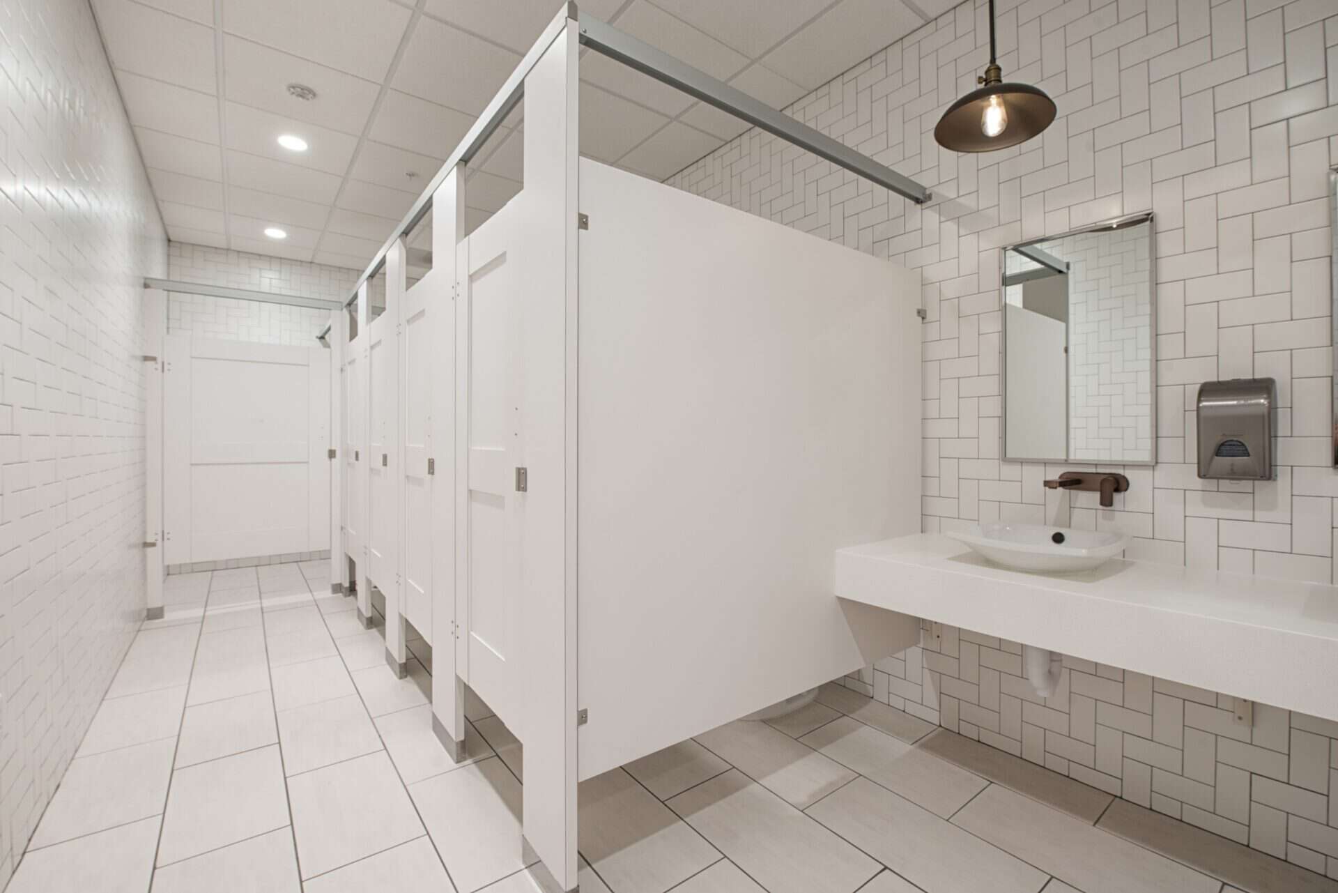 A modern restroom with white high pressure laminate partitions with captured panels and headrail braced mounting.