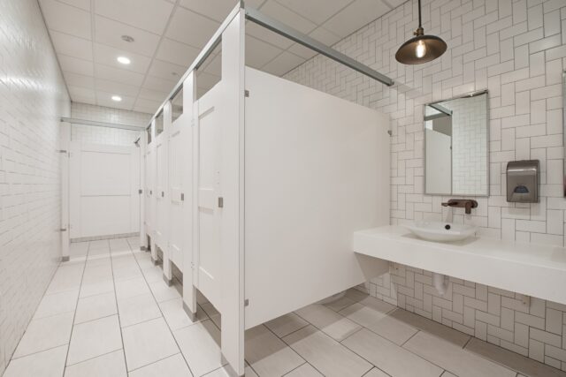 A modern restroom with white high pressure laminate partitions with captured panels and headrail braced mounting.