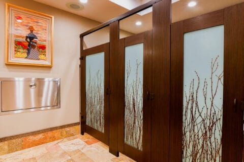 A restroom with three stalls made of high pressure laminate, mounted with powder coated headrail bracing, and with 3form acrylic door lites.