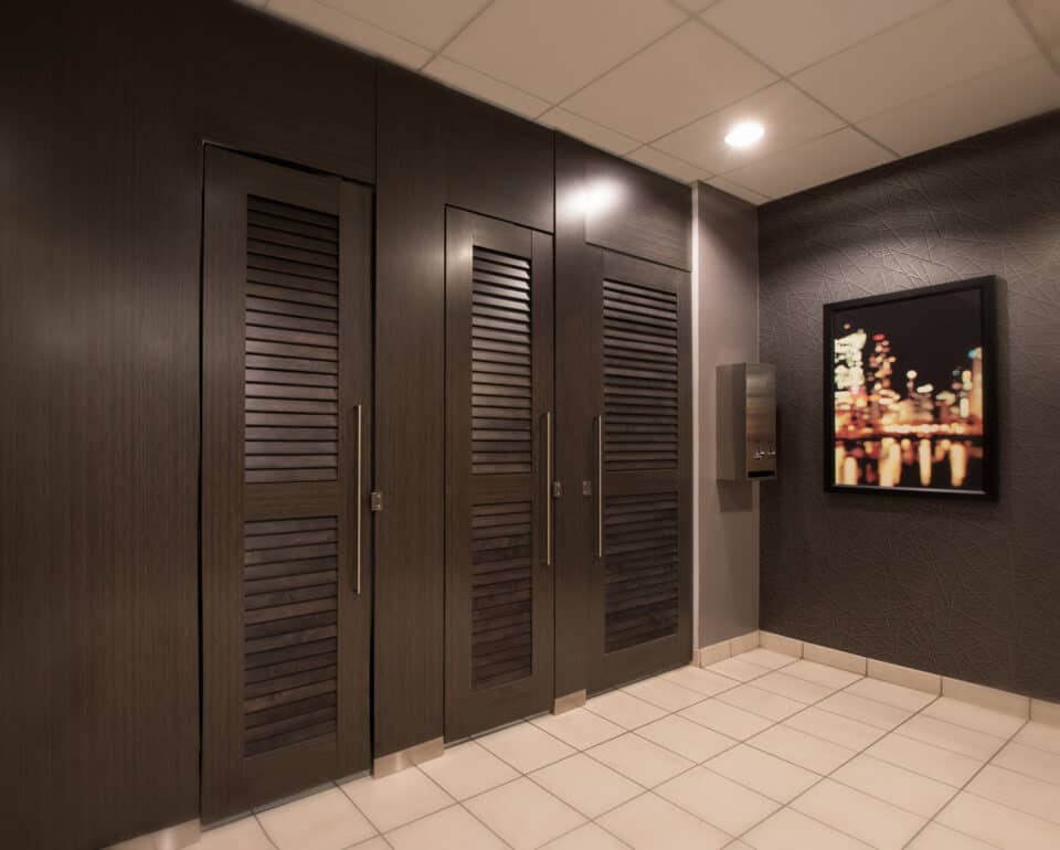 Commercial restroom with modern high pressure laminate louvered partitions with long pulls and transoms. Floor to ceiling mount. Picture on the right.