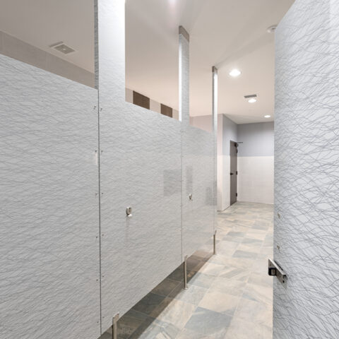 Public restroom with light gray patterned high pressure laminate stalls with pedestals at the bottom.