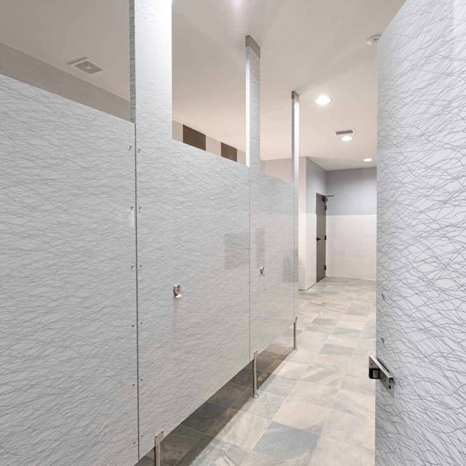 Public restroom with light gray patterned high pressure laminate stalls with pedestals at the bottom.