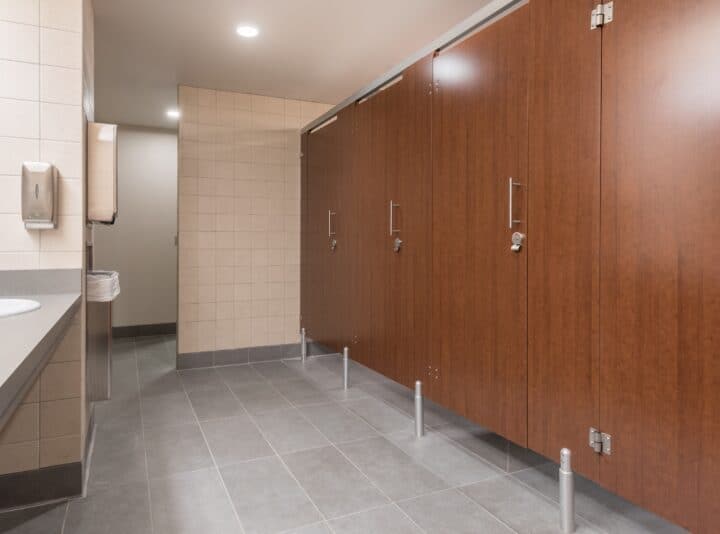 European style commercial restroom with high-privacy plastic laminate partitions, aluminum pedestals, headrail bracing, and stainless steel hardware.