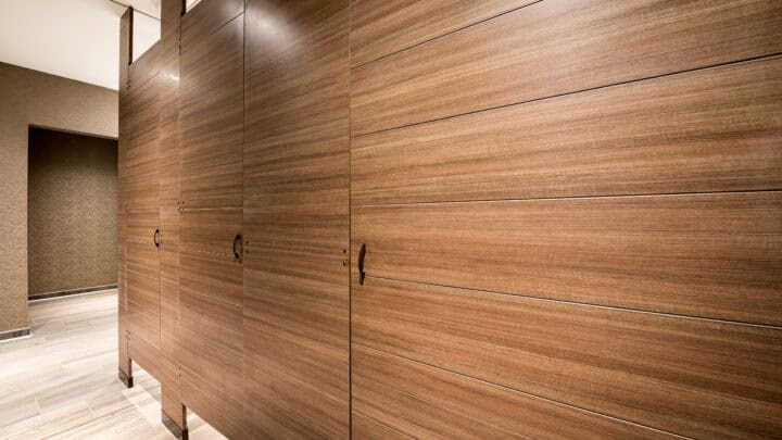 Three toilet partitions in a woodgrain laminate, oriented horizontally, with engraving and floor to ceiling mount.