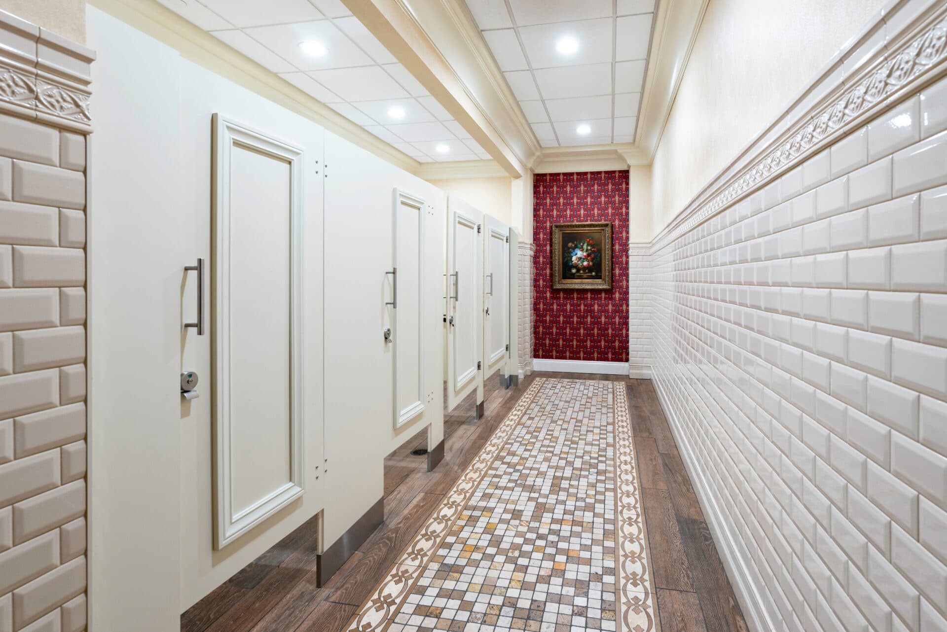 Headrail-braced restroom partitions in a hotel, featuring compact laminate panels in Natural Almond with applied molding, brushed satin hardware, and bar pulls.