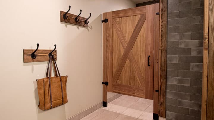 A bathroom with a wooden barn-style door, tiled shower walls, hooks with a bag, and a sink with a countertop and towels.