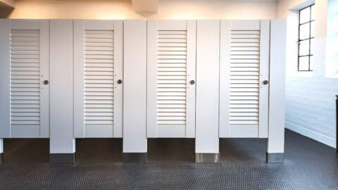 Restroom partitions with white louver doors and floor-mounted design, providing privacy and improved airflow for commercial restroom installations