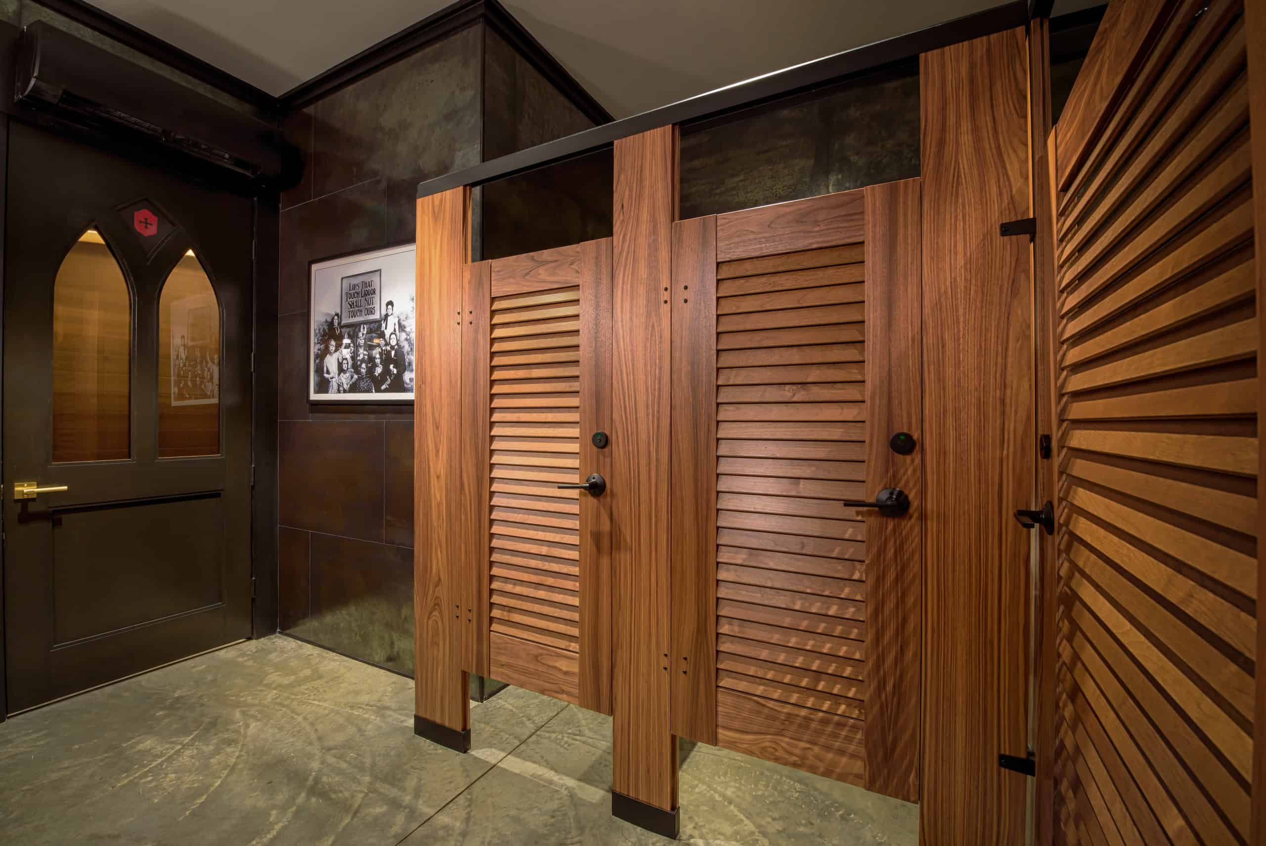 A restroom with wooden stall doors and black hardware, an exterior-style black door, and a framed black-and-white photo on the wall.