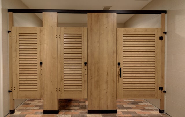 Full view of commercial restroom partitions with louvered woodgrain doors and black hardware, installed at Lancaster Country Club