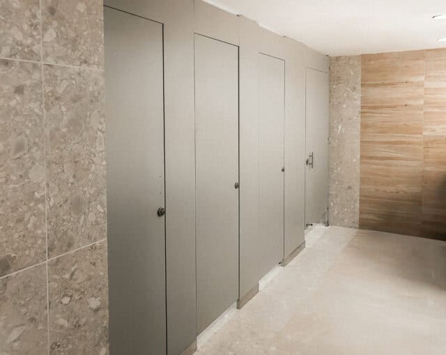 Four closed restroom stalls with light-colored doors, set against tiled and wooden walls in a clean, modern bathroom.