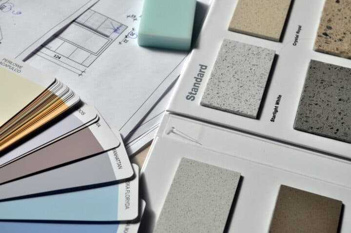 A collection of color swatches, architectural plans, and stone samples on a table, with a blue eraser placed on the plans.