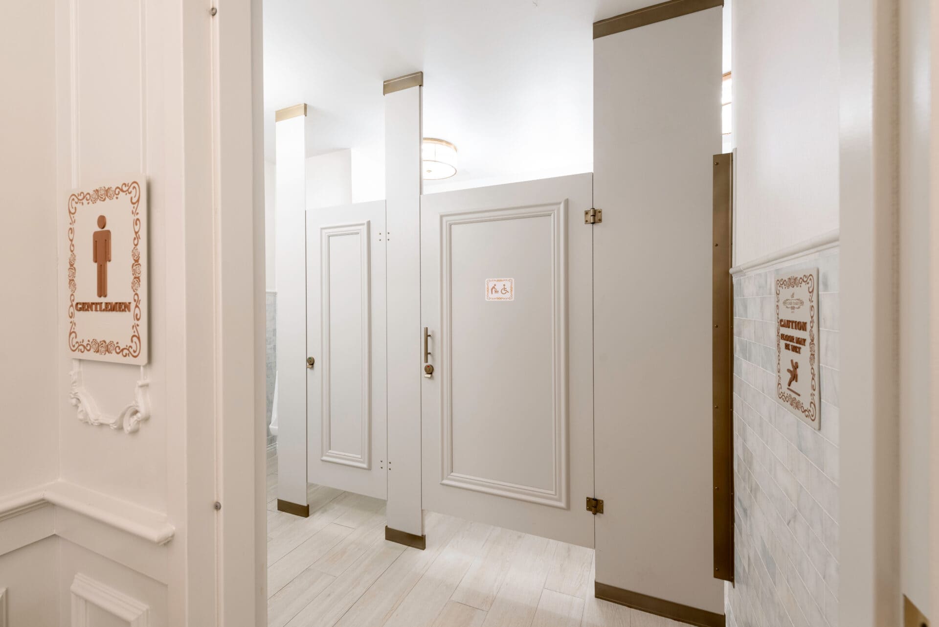Floor-to-ceiling restroom partitions in a high-end Florida restaurant men's room, featuring compact laminate in Frosty White with applied molding and powder-coated brass metallic hardware.
