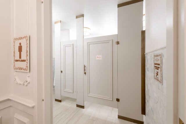 Floor-to-ceiling restroom partitions in a high-end Florida restaurant men's room, featuring compact laminate in Frosty White with applied molding and powder-coated brass metallic hardware.