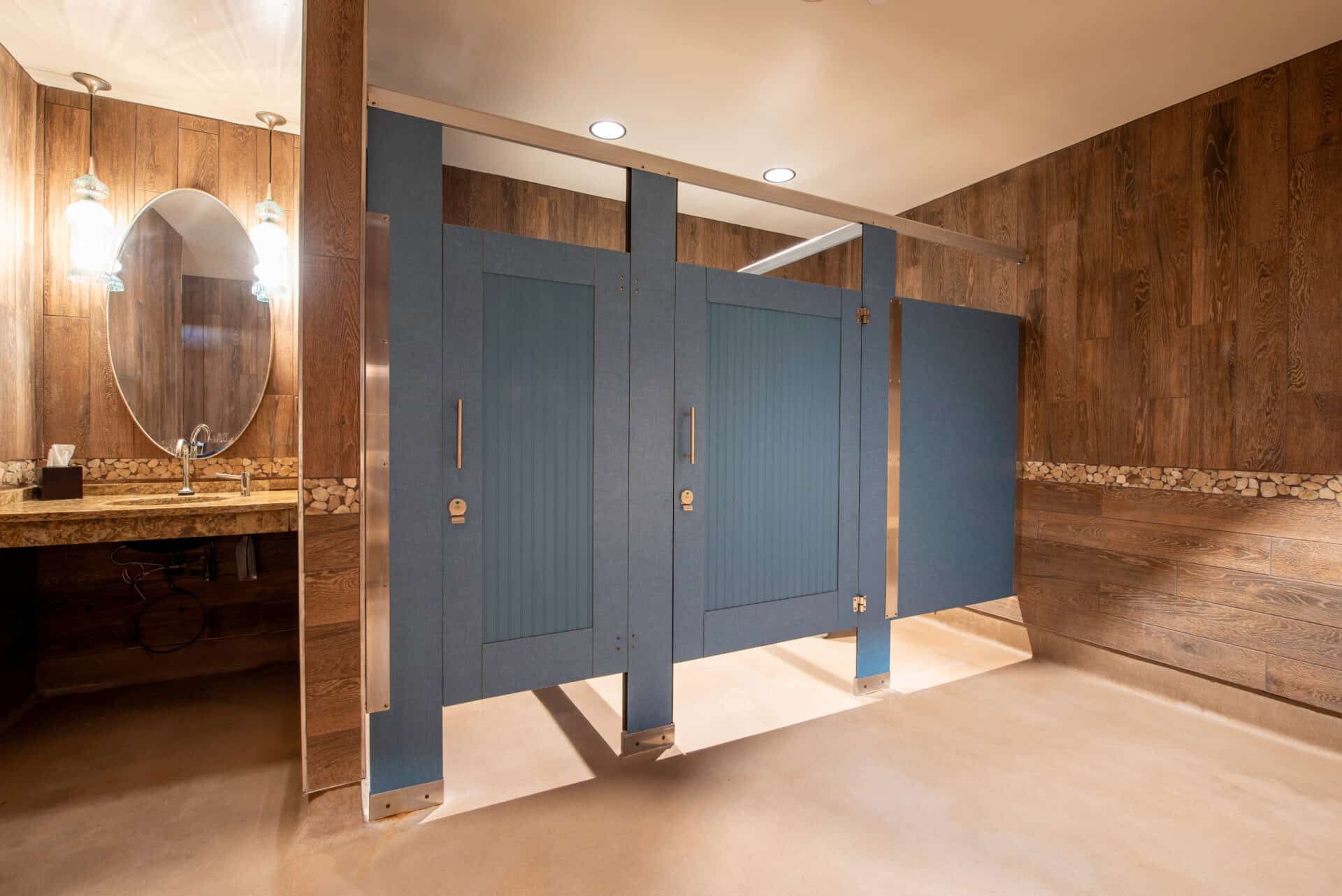 Restroom partitions in dark blue compact laminate with vertical beadboard-style captured panel doors and stainless steel hardware in a headrail-braced configuration.
