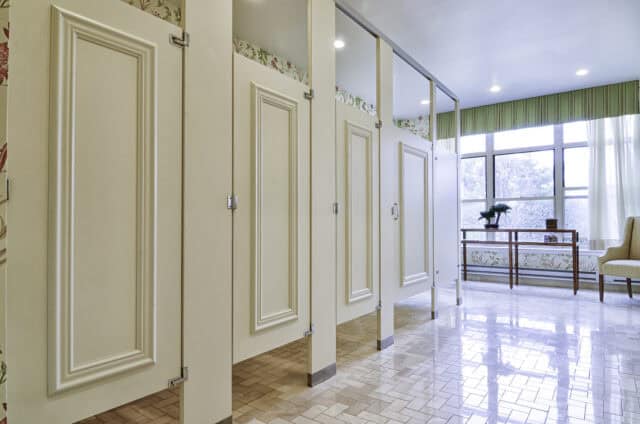 Molding-style painted laminate restroom partitions in a bright senior center restroom with large windows and floral accents.