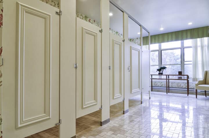 Molding-style painted laminate restroom partitions in a bright senior center restroom with large windows and floral accents.