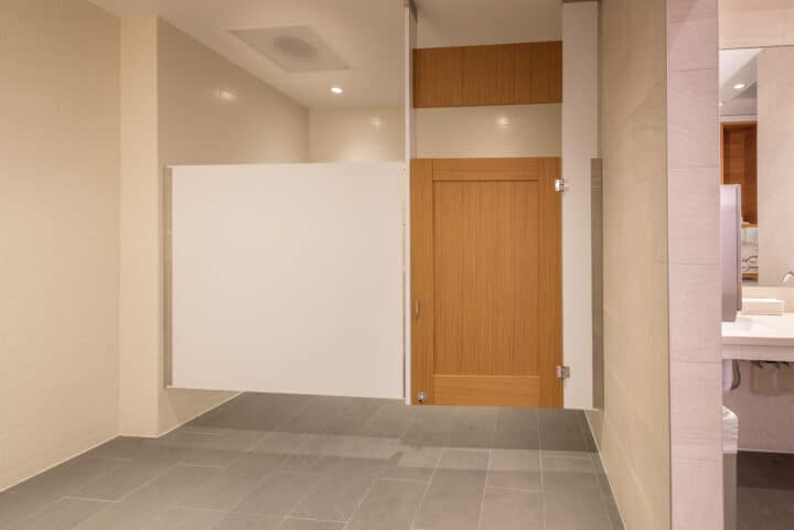 A public restroom with a treefrog wood veneer door and high pressure laminate panel and pilasters and a stabilizing transom.