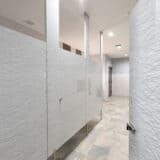 Public restroom with light gray patterned high pressure laminate stalls with pedestals at the bottom.