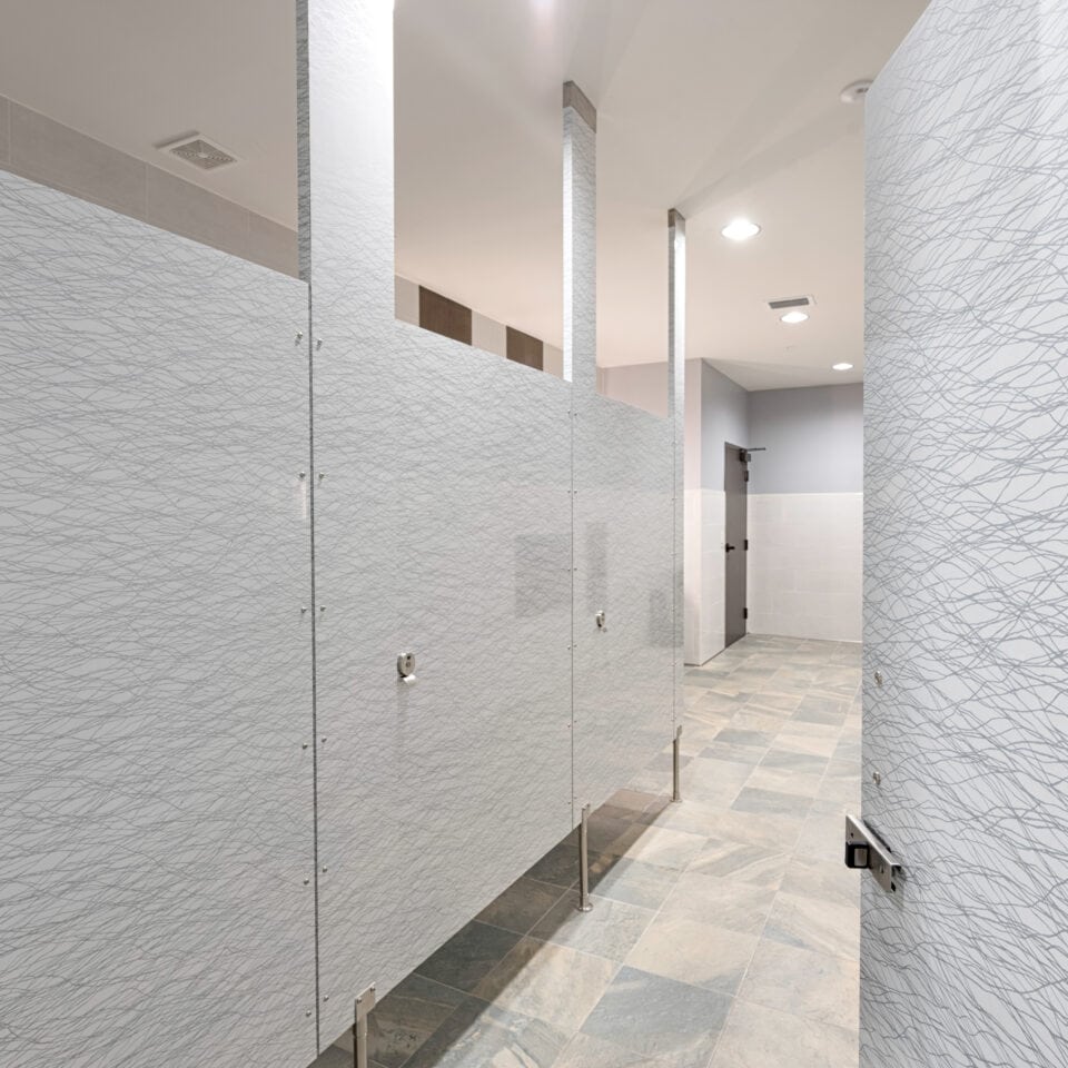 Public restroom with light gray patterned high pressure laminate stalls with pedestals at the bottom.