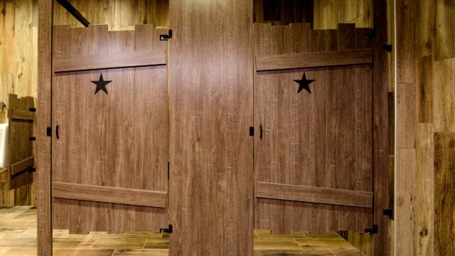 Rustic bathroom stall doors with heart cutouts, wooden planks, and metal hinges in a whitewashed interior.