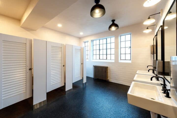 Floor-mounted bathroom partitions with white louvered doors, and stainless steel hardware.