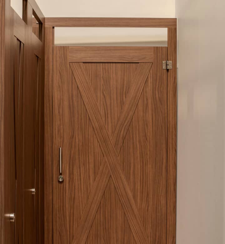 A wood veneer toilet partition with "barn x" type applied moldings and Ironwood Manufacturing Zero Sightline privacy.