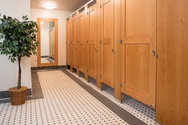 A row of upscale public restroom partitions made of wood veneer with captured panel doors, midrails, and headrail braced mounting.