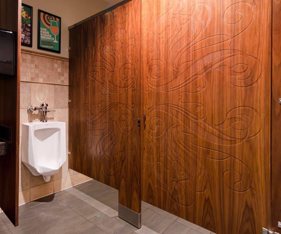 Men's restroom with a urinal on the left and an upscale restroom partition in wood veneer with engravings on the right.