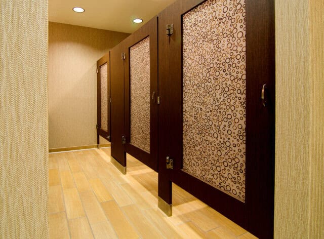 A restroom with stalls made of wood veneer, floor mounted, with 3form acrylic door lites.