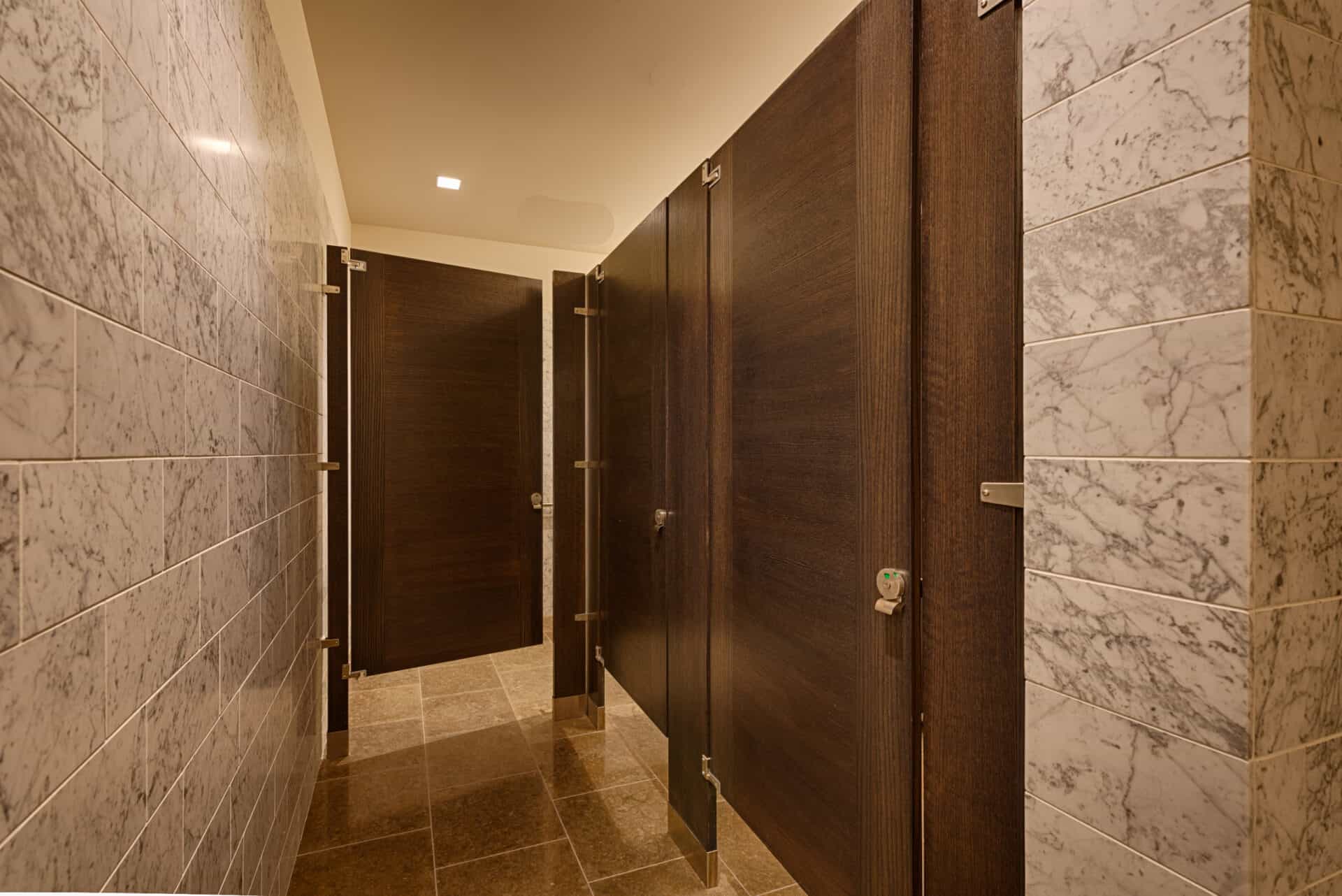 A commercial upscale restroom featuring wood veneer inlay doors (sketch face). Floor mounted with stone tile walls.