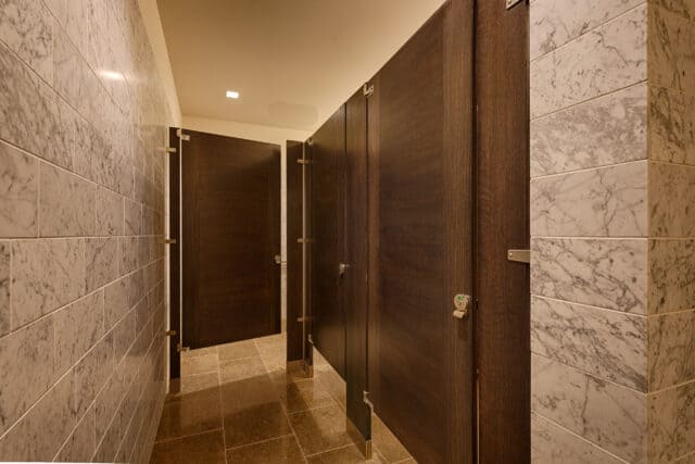 A commercial upscale restroom featuring wood veneer inlay doors (sketch face). Floor mounted with stone tile walls.