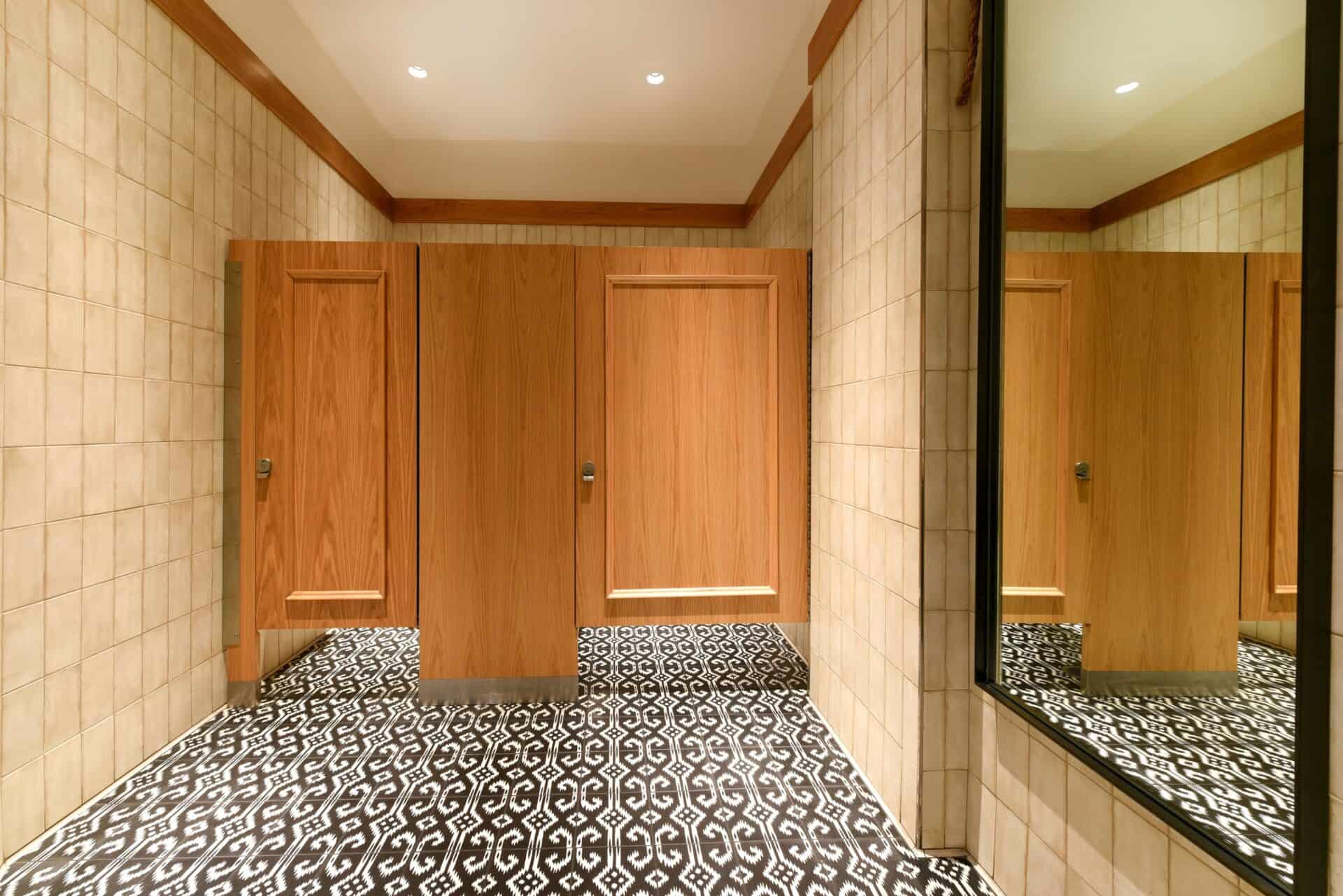 A commercial restroom with two partitions in wood veneer, floor mounted, with applied moldings on the doors.