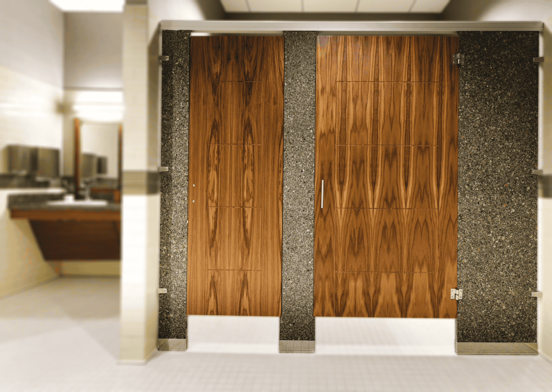 Two upscale public restroom partitions with engineered stone pilasters, engraved wood veneer doors, and headrail bracing.