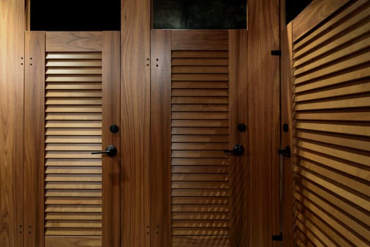 Louvered wood veneer toilet partitions with the Ironwood Zero Sightline lapped component feature in a commercial restroom