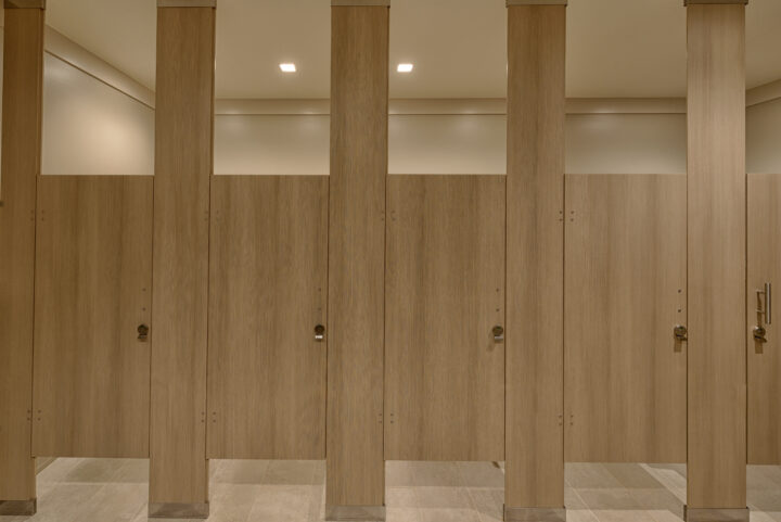 A row of woodgrain compact laminate toilet partitions mounted floor to ceiling with Ironwood Manufacturing's Zero Sightline feature.